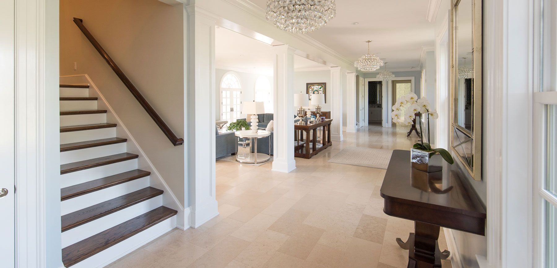 Elegant entry hall with a staircase, chandelier, and hallway leading to a living room.