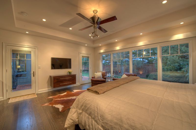 Cozy bedroom with a large bed, TV, and floor-to-ceiling windows overlooking a backyard.