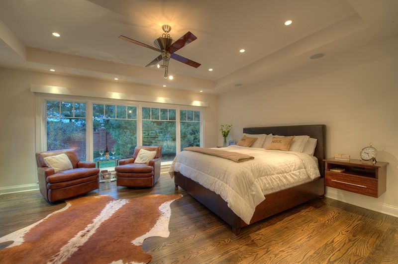 Bedroom with bed, armchairs, cowhide rug, and large windows overlooking a yard.