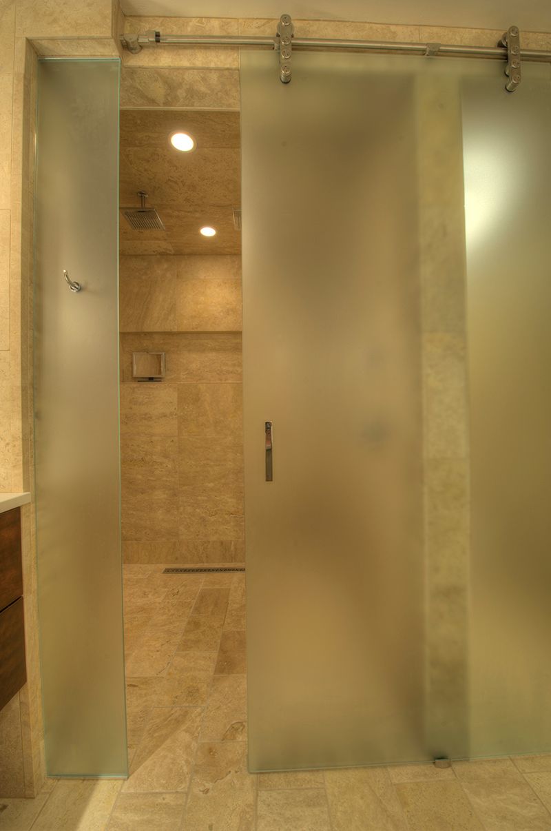Frosted glass sliding shower door; inside is a tiled shower stall, light fixtures.