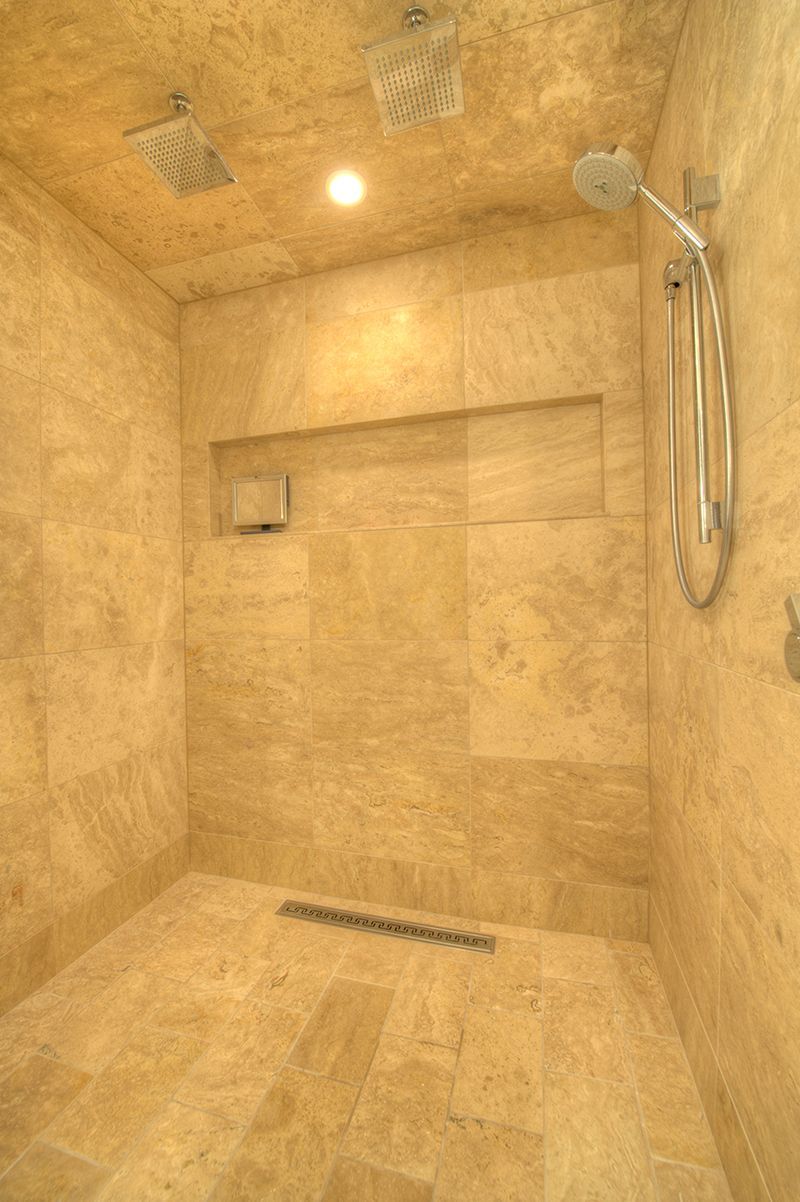 A beige tiled shower with a hand shower, built-in shelf, and drain.