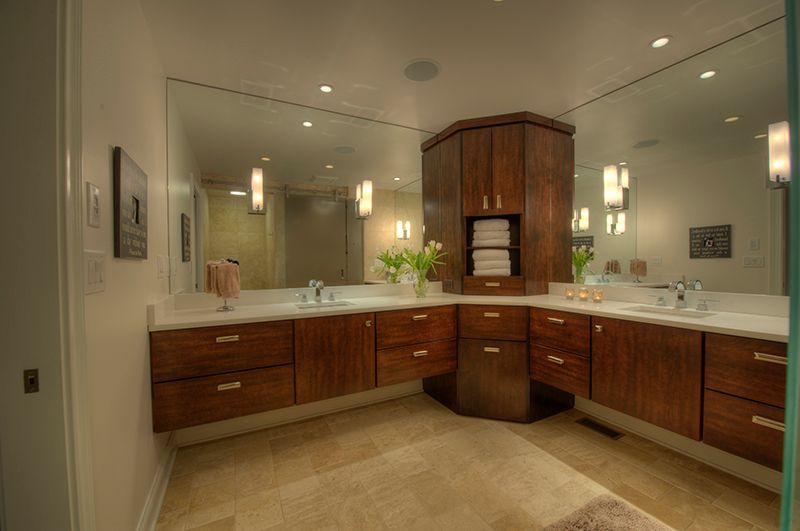Modern bathroom with wooden cabinets, large mirrors, and white countertops.
