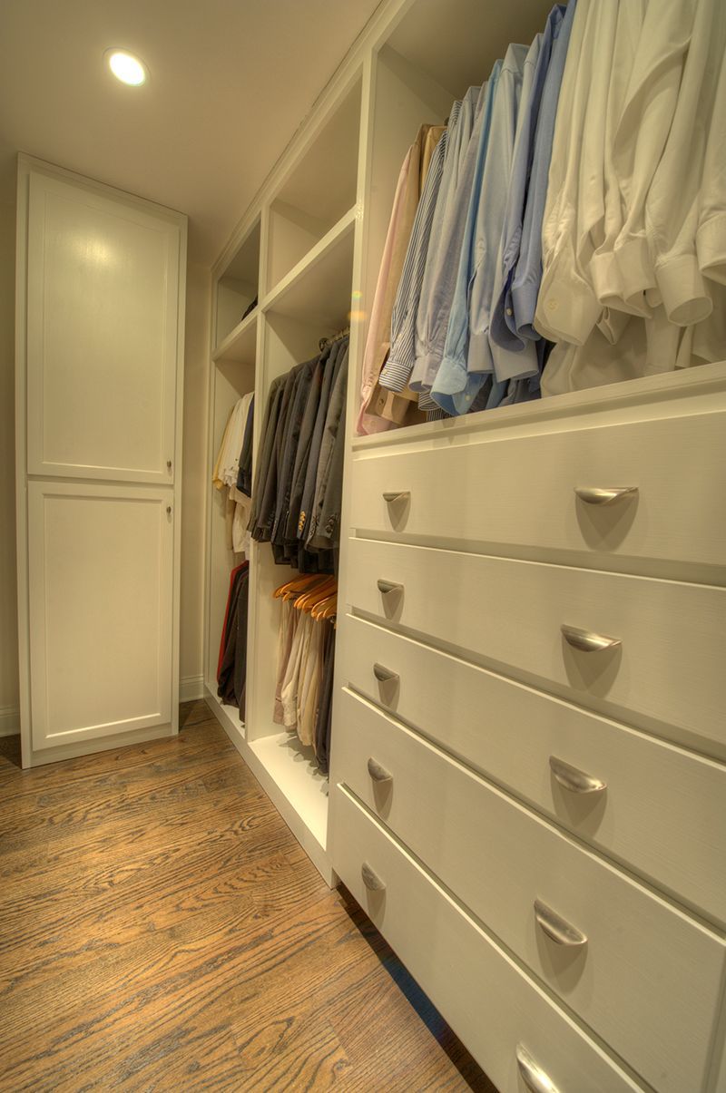White closet with drawers, hanging clothes, and wood floor.