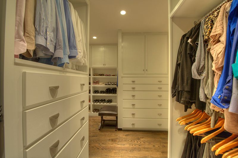 A walk-in closet with white drawers and cabinets, clothing racks, and hardwood floors.