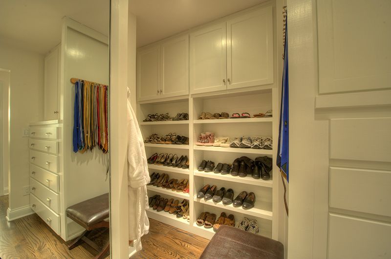 Walk-in closet with built-in shoe shelves, bench, and mirror, all white, with a robe and ties.