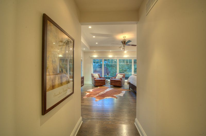 Hallway leading to a bedroom with chairs and large windows; art on the left wall.