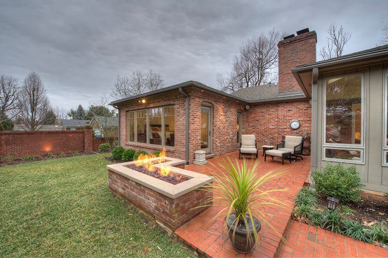 Backyard patio with fire pit, brick buildings, chairs, and lawn on a cloudy day.