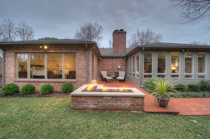 Brick patio with fire pit, seating, and house; overcast sky.