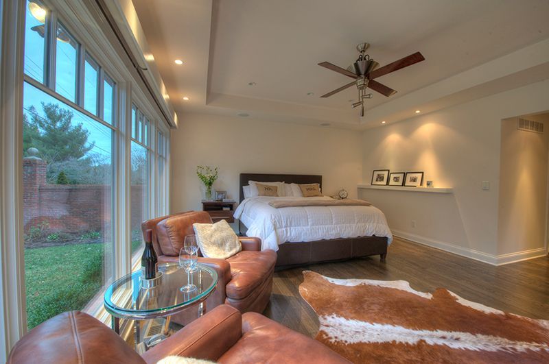 Bedroom with large windows, brown leather chairs, bed, and cowhide rug.