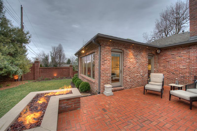 Brick patio with a fire pit and seating next to a brick house on a cloudy day.