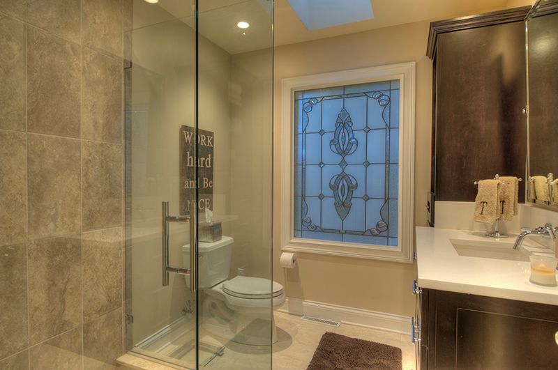 Bathroom with glass shower, toilet, dark cabinets, decorative window, and white countertops.