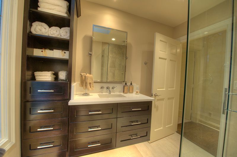 Dark wood bathroom vanity with built-in storage, white towels, sink, mirror, and light-colored floor.