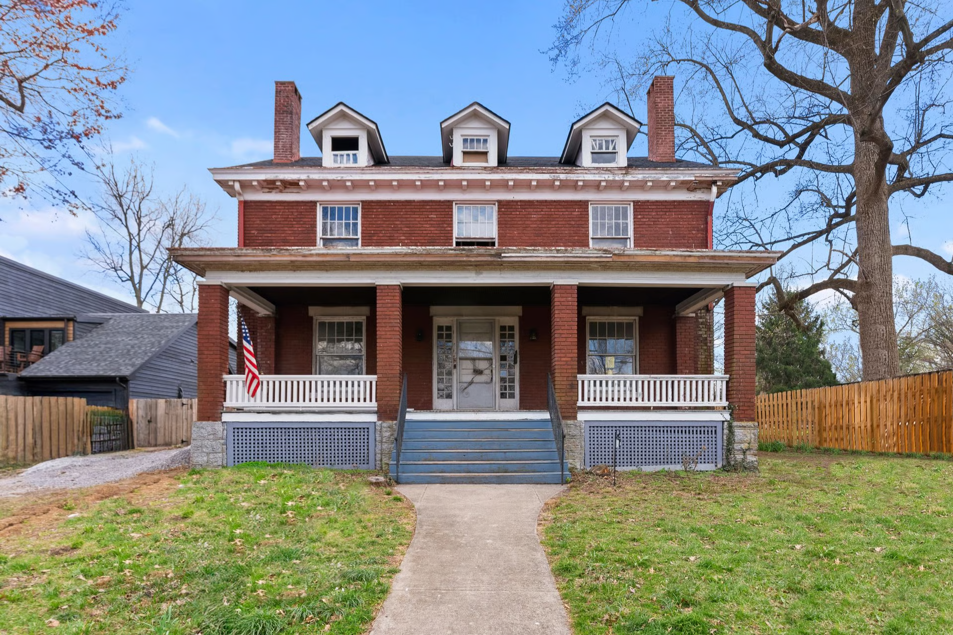 Red brick house with porch, columns, and three dormers. American flag on porch.
