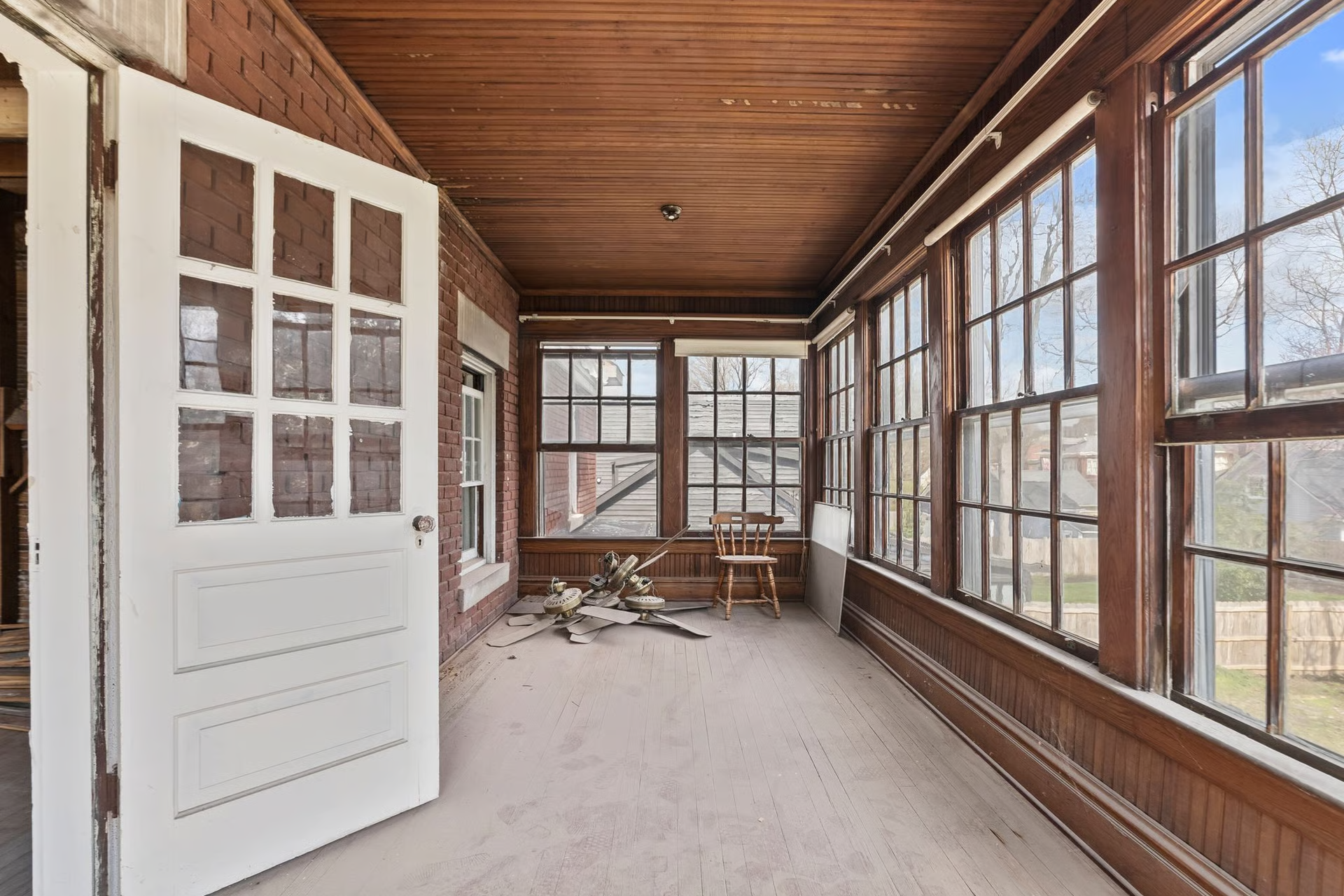 Sunroom with wooden trim, many windows, and a white door. Debris on the floor.