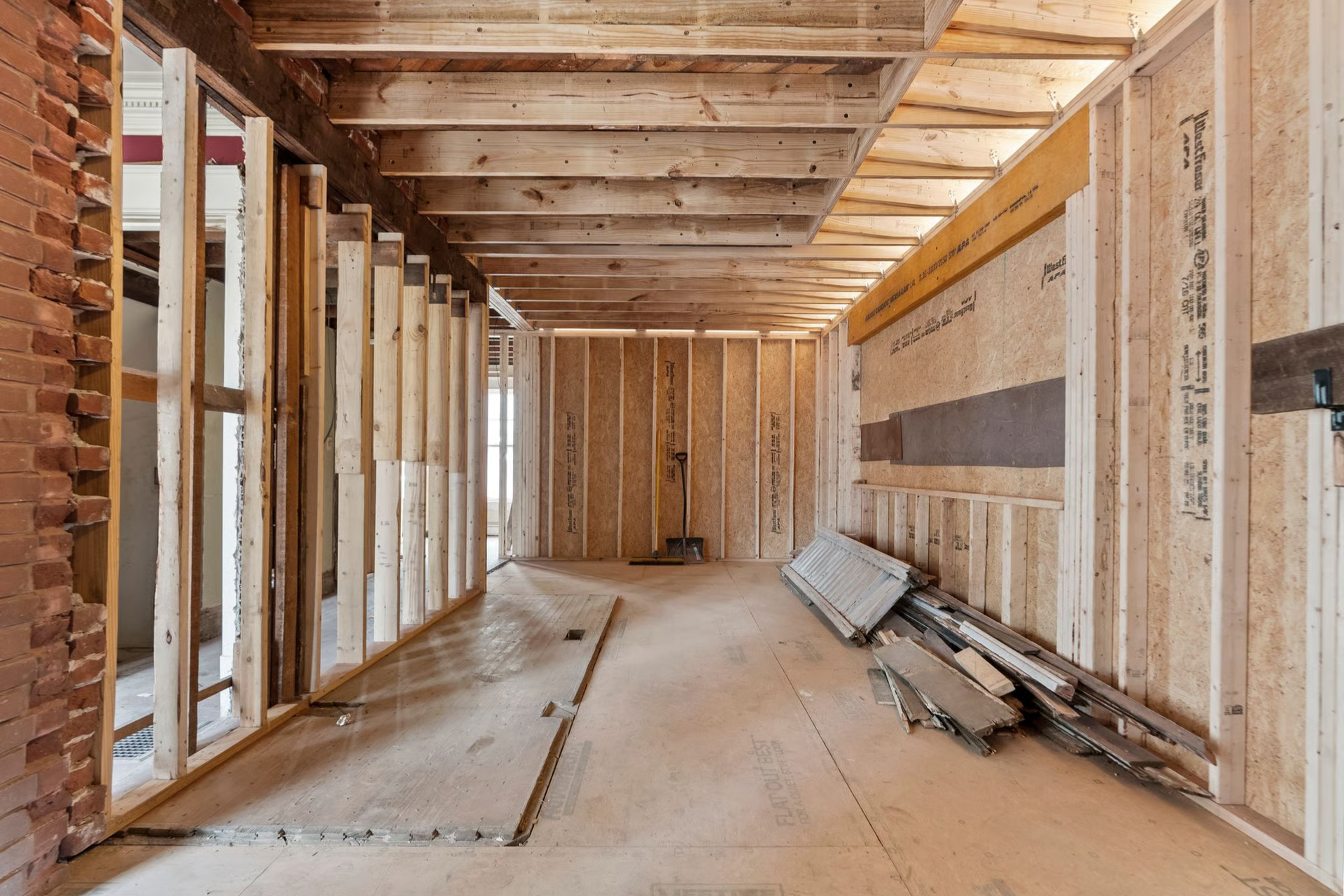 Interior construction site with exposed wooden framing and brick wall.