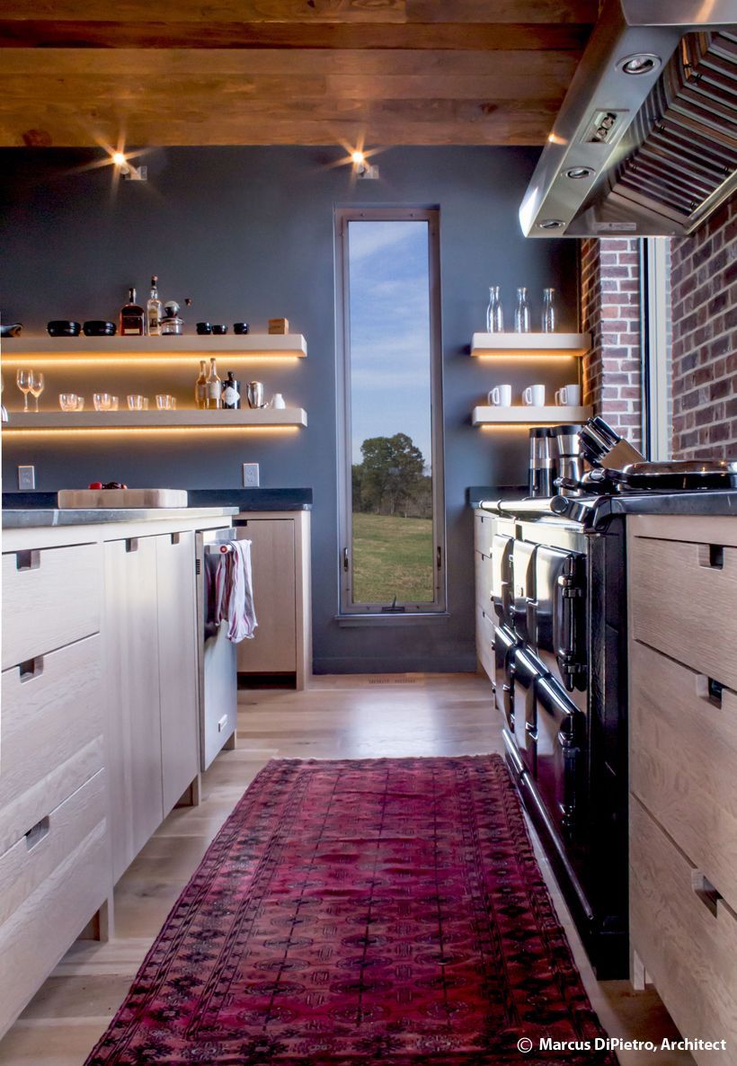 Modern kitchen with light cabinets, a red rug, and a tall window overlooking a green field.