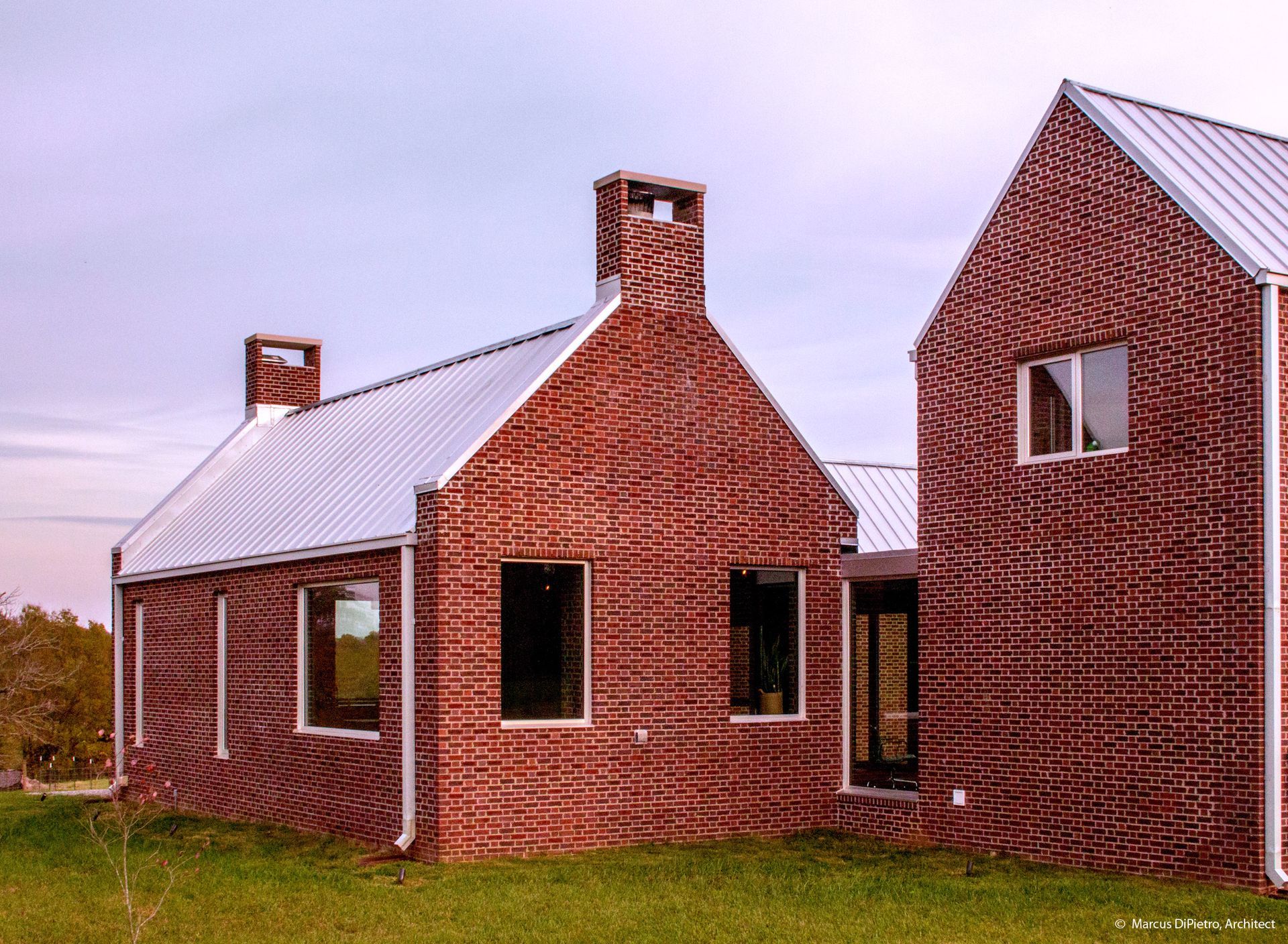 Brick house with a patterned facade, metal roof, and chimney. Windows and grass.