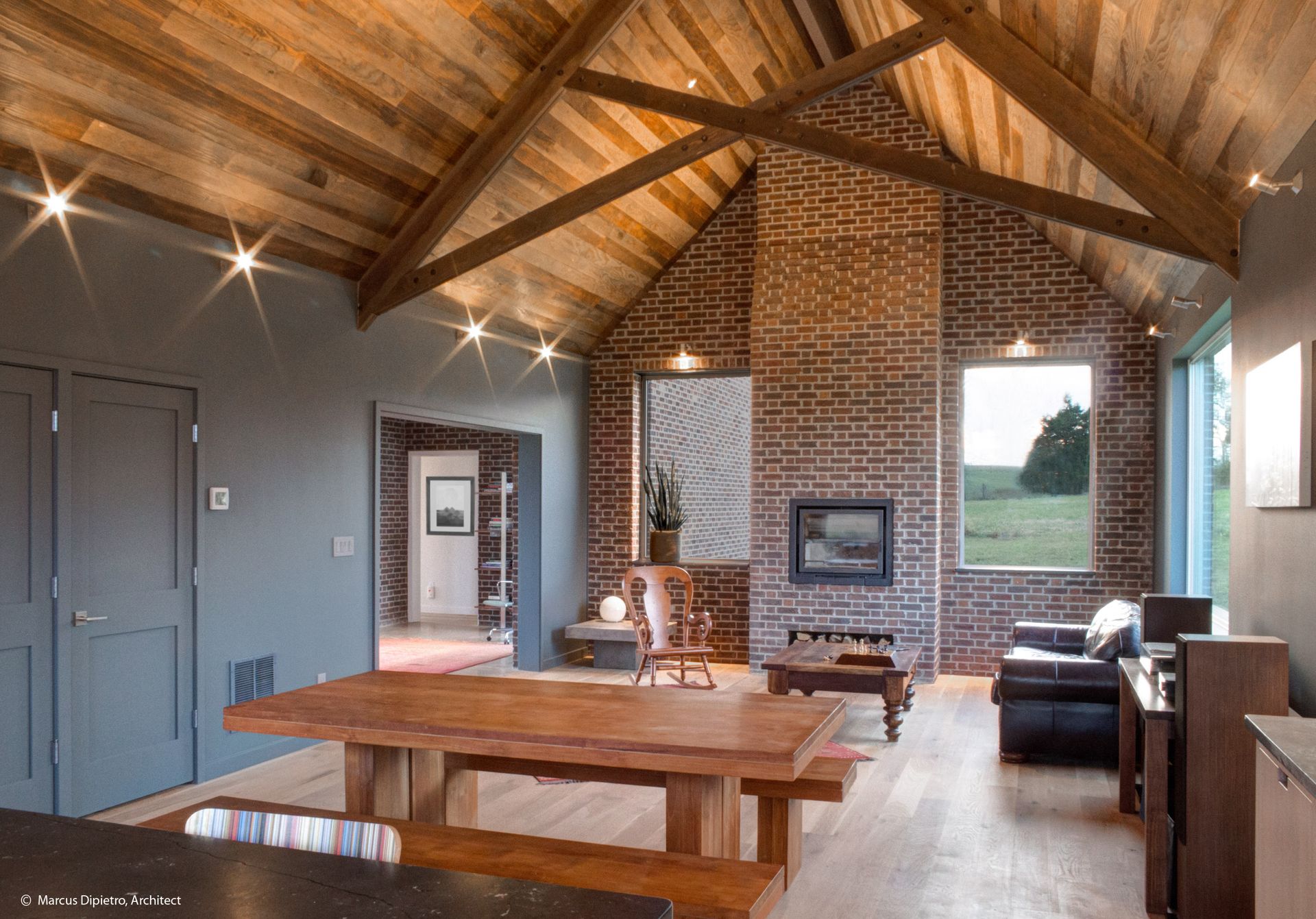 Rustic interior with wood ceiling, brick fireplace, and large wooden table.