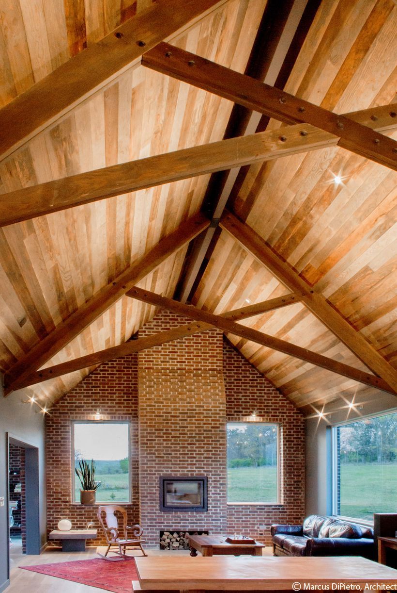 Wooden ceiling with exposed beams, brick fireplace, windows, and living room furniture.