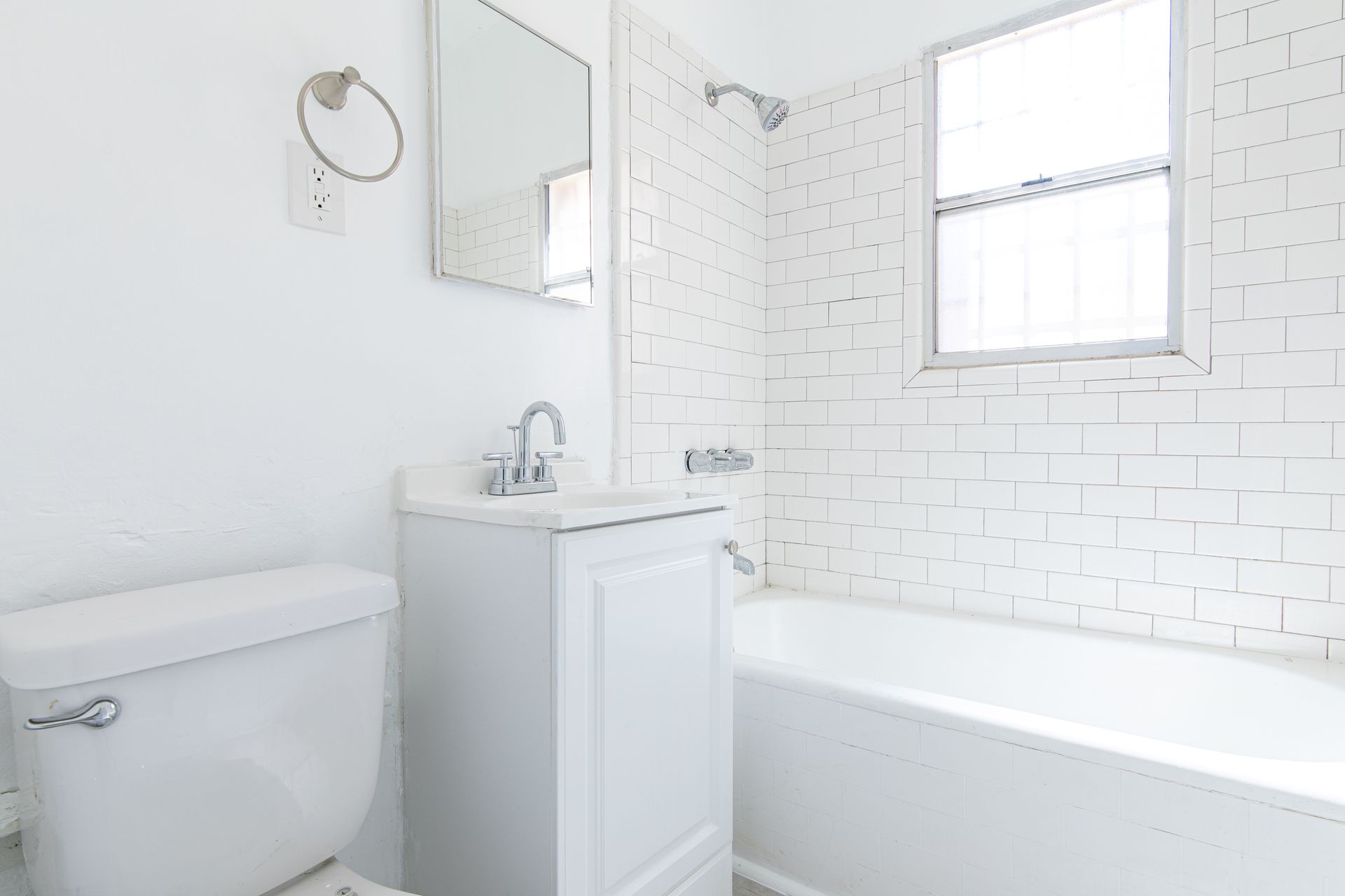 White bathroom with a toilet, sink, mirror, and bathtub.