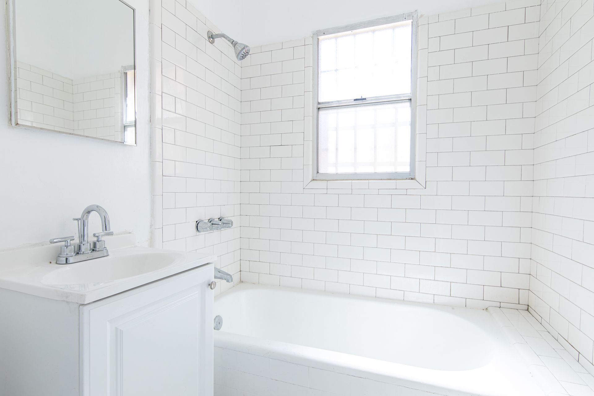 White bathroom with tiled walls, bathtub, sink, mirror, and window.