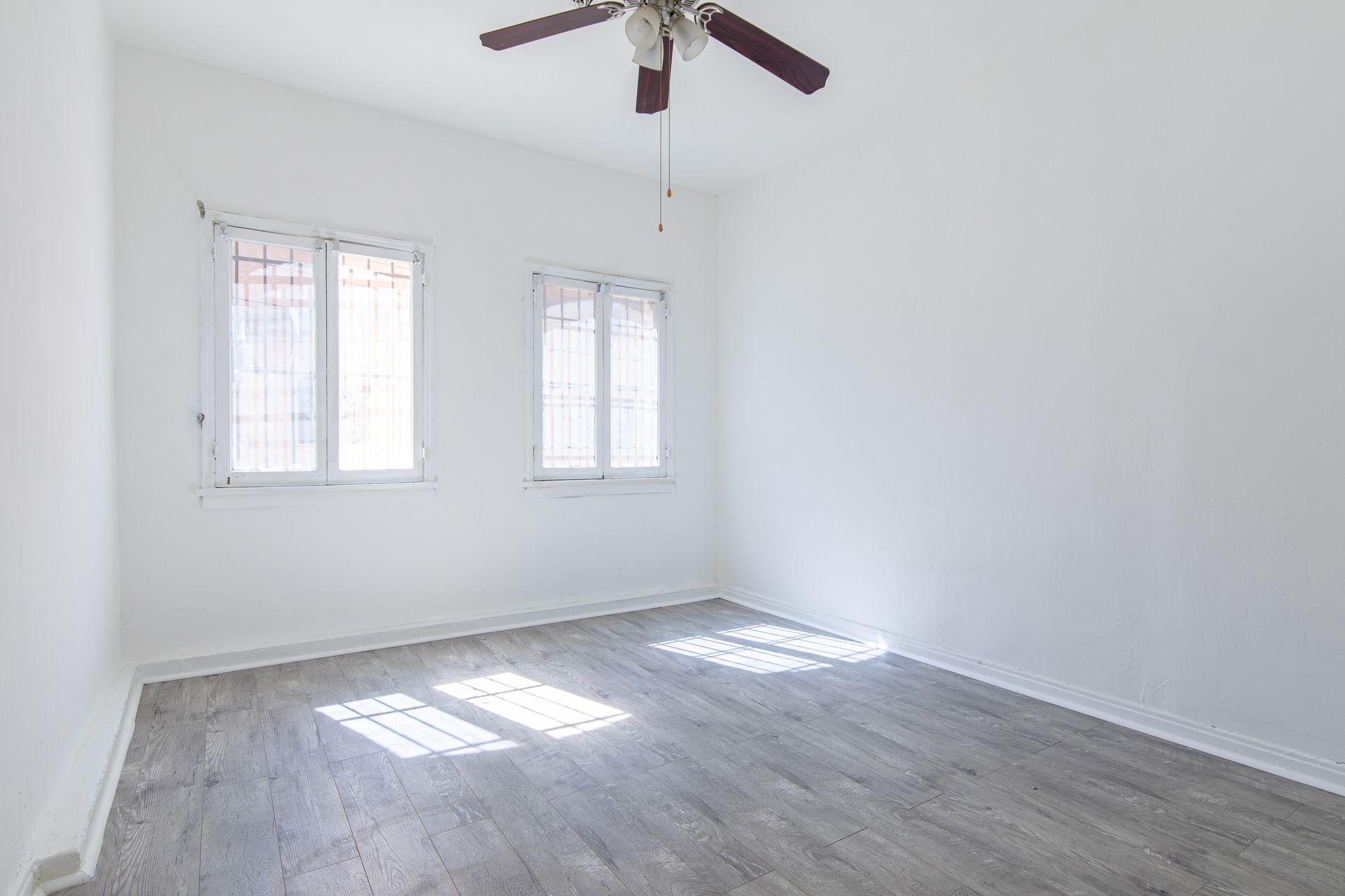 Empty room with white walls, two windows, gray flooring, and a ceiling fan.