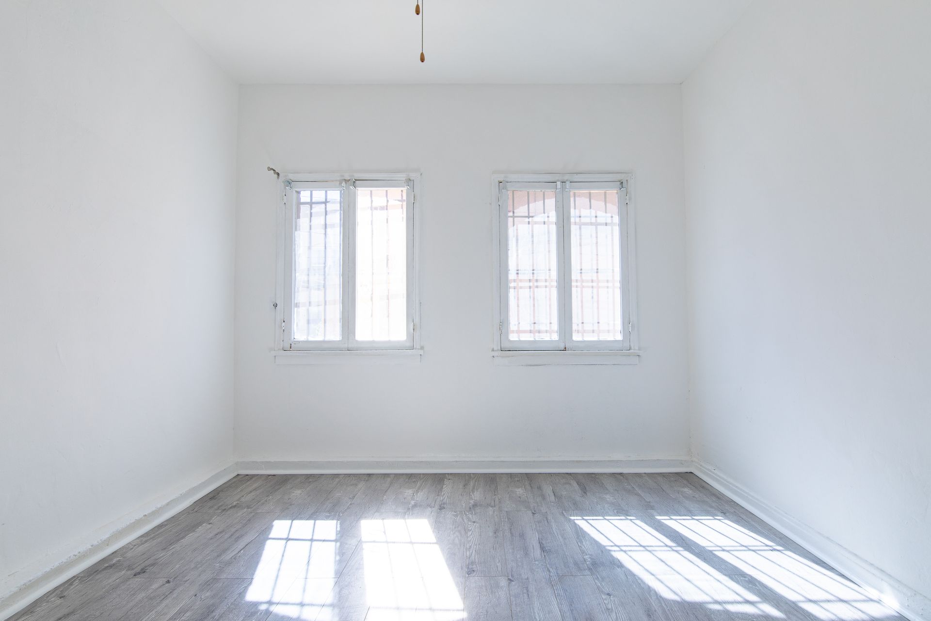Empty white room with two windows, gray floor, and natural light.
