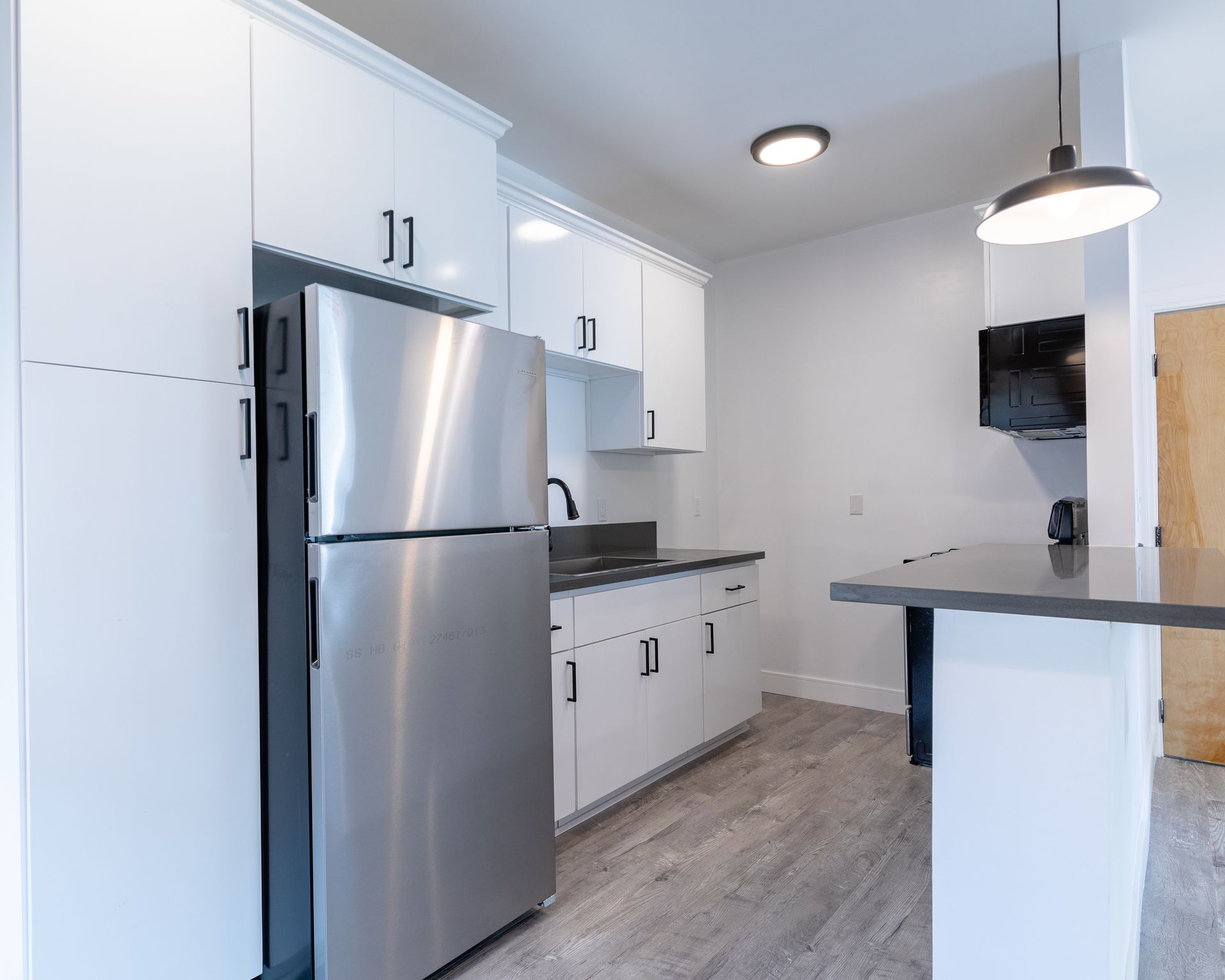 Modern kitchen with stainless steel refrigerator, white cabinets, and gray countertops.