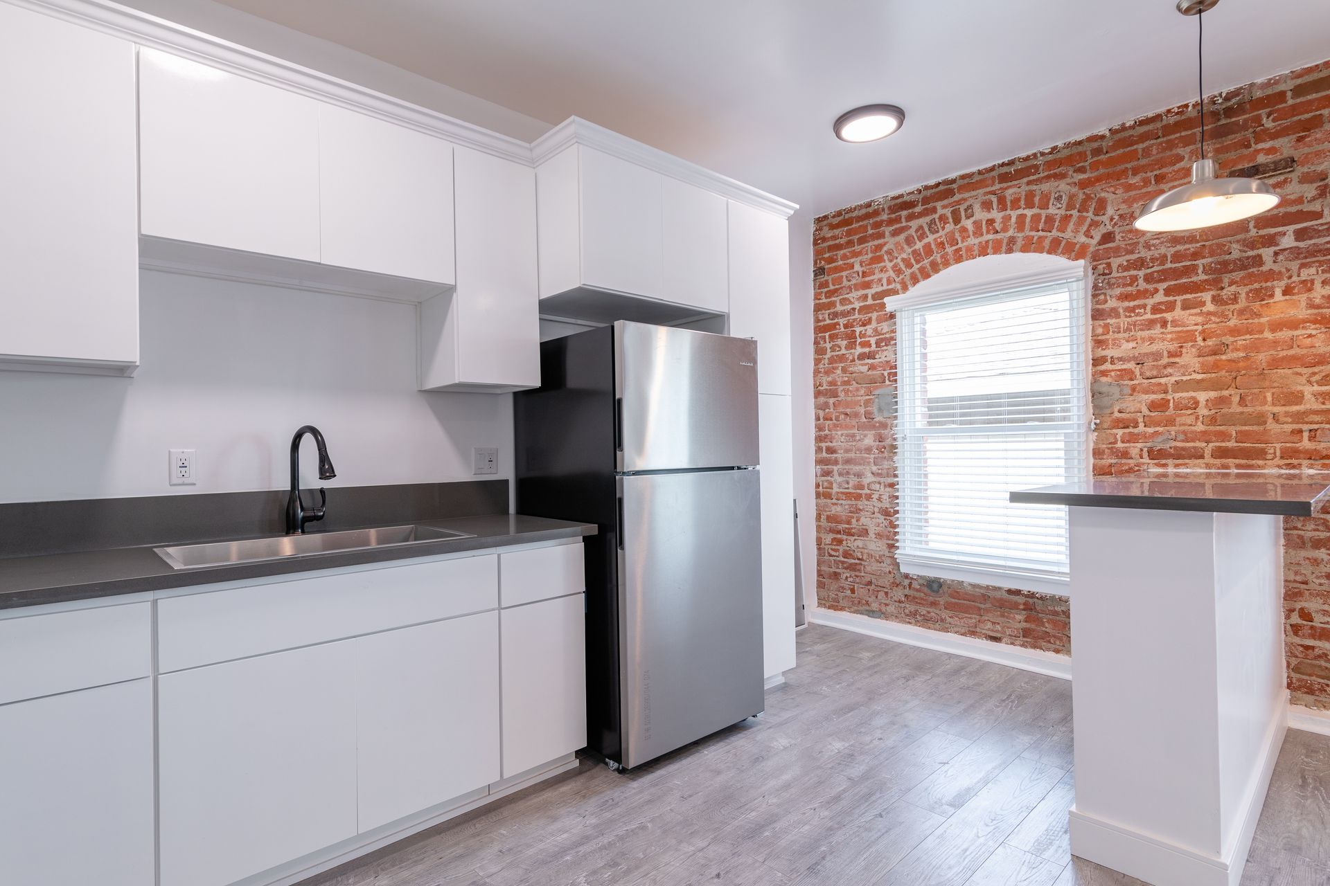 Modern kitchen with white cabinets, stainless steel fridge, brick wall, and breakfast bar.