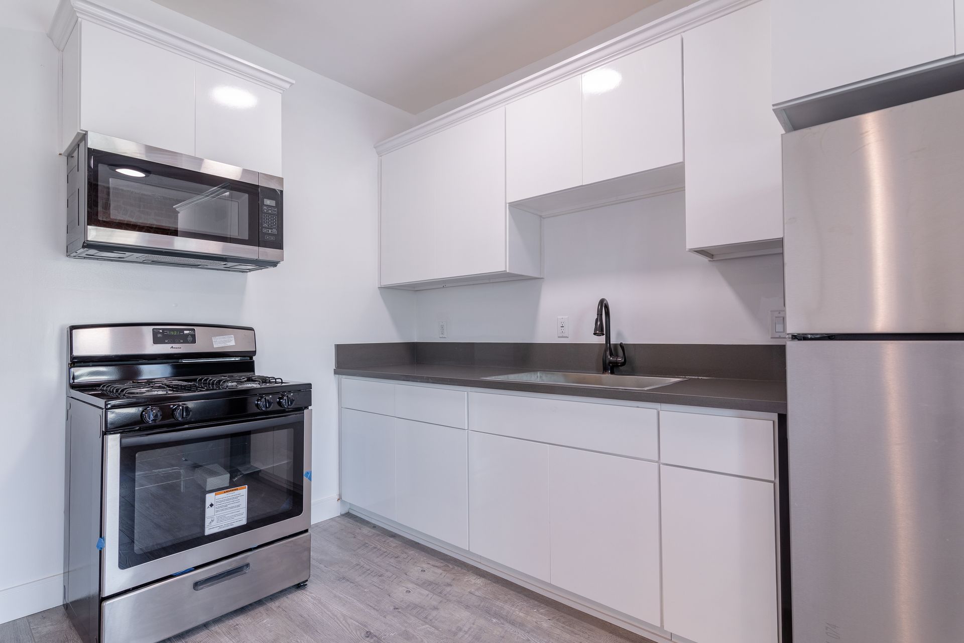 Modern white kitchen with stainless steel appliances: microwave, stove, and refrigerator.