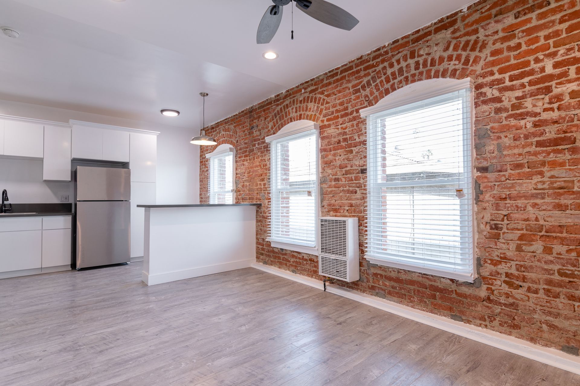 Interior of a renovated loft with exposed brick wall, white kitchen cabinets, and two arched windows.