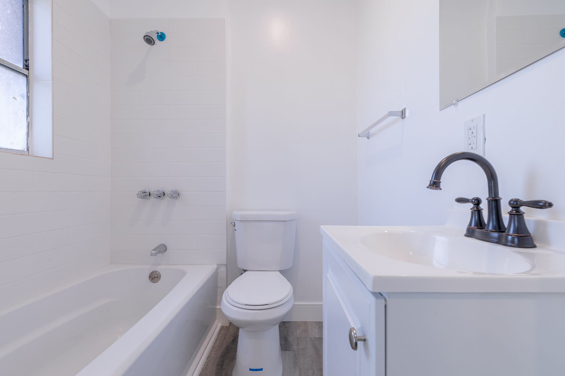 White bathroom with tub, toilet, and vanity. Black faucet, silver towel rack, light gray floor.