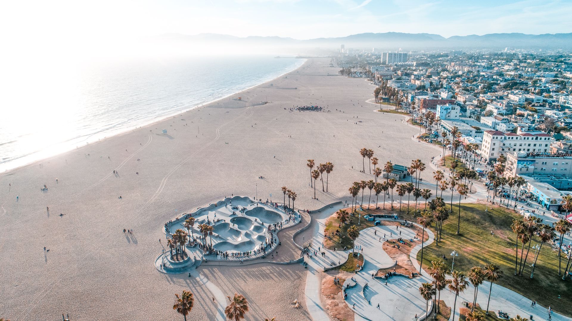 Aerial view of Venice Beach, California, with a skate park, sand, ocean, and buildings on a sunny day.