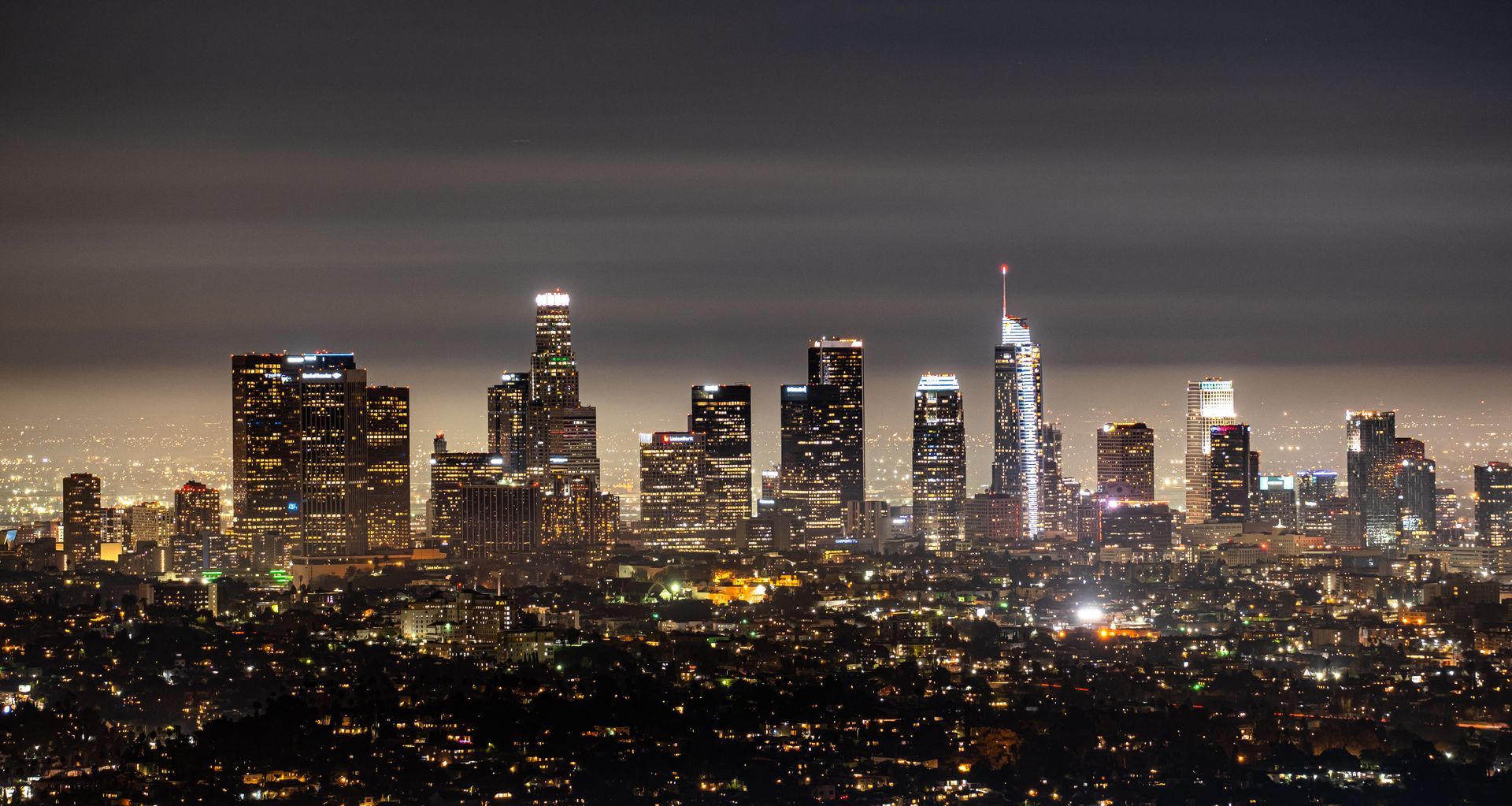 Night view of Los Angeles skyline, illuminated against a dark sky with city lights below.