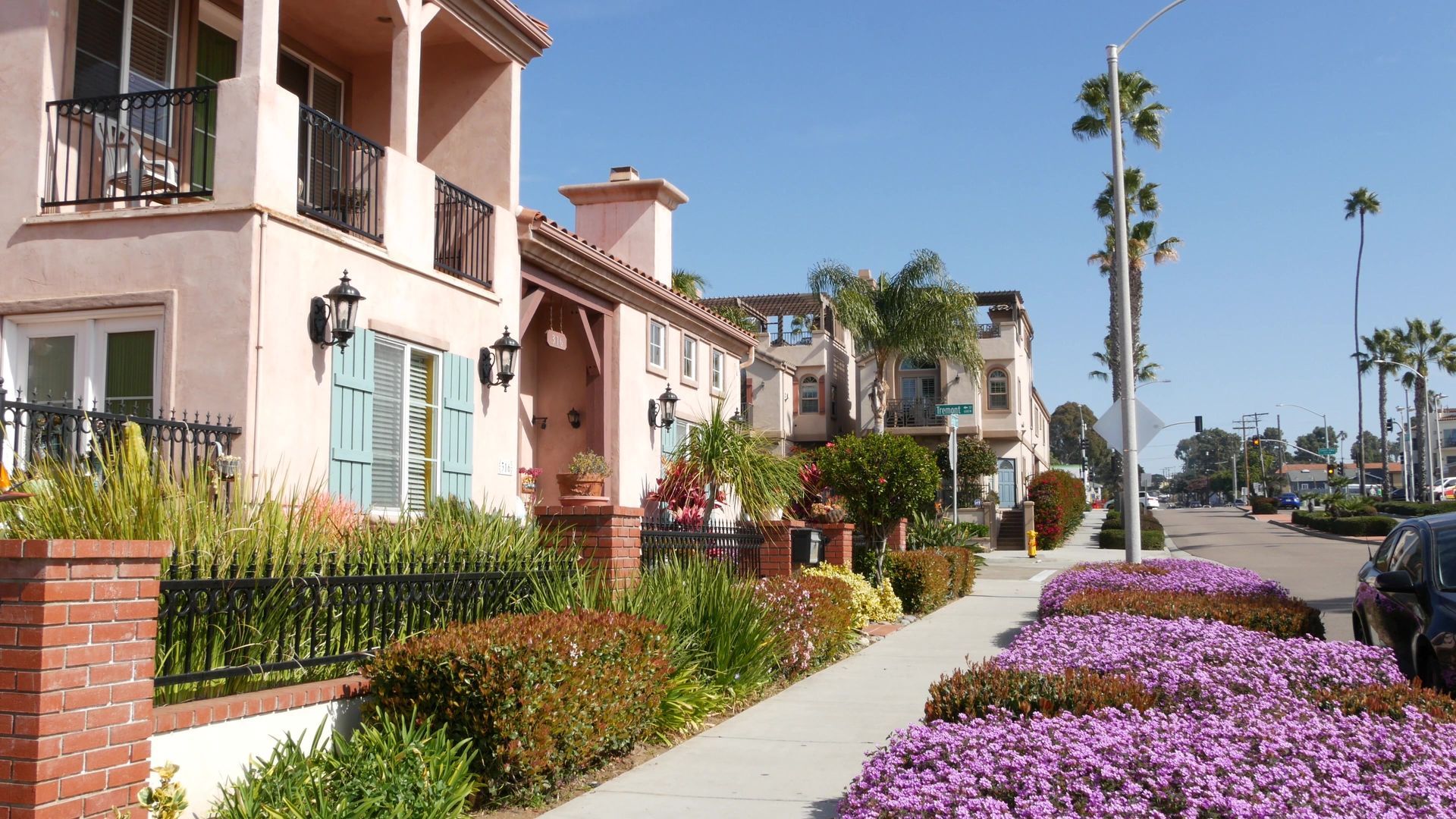 Townhouses with pink stucco exteriors and colorful landscaping line a sunny street.