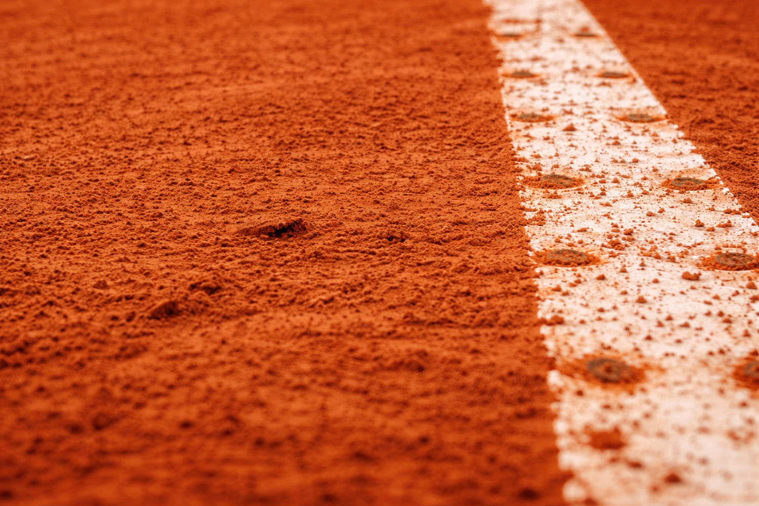 Una vista ravvicinata e angolata di una linea bianca di un campo da tennis su una superficie di terra battuta ruvida, di colore rosso-arancio.