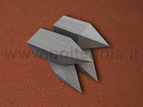 Tre paletti di metallo grigio con punte appuntite a forma di scalpello, disposti su una superficie ruvida di colore bruno-rossastro.