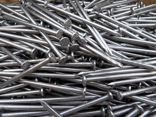 Un grande e caotico mucchio di chiodi di metallo color argento con testa piatta, impilati uno sull'altro.