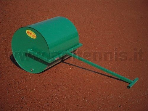 Un rullo da giardino manuale verde è appoggiato su un campo da tennis in terra battuta rossa.