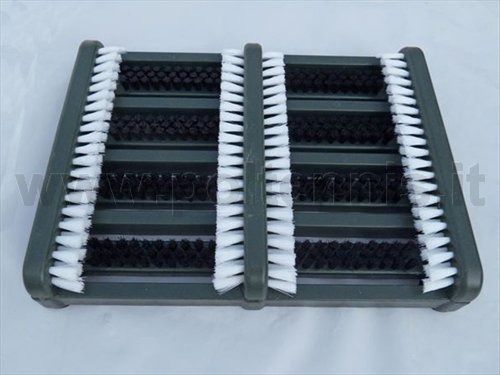 Una spazzola per la pulizia delle scarpe con tre file verticali di setole bianche e strisce abrasive nere su una struttura grigio scuro.