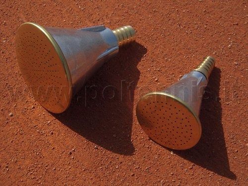 Due teste di annaffiatoio in metallo con superfici in ottone e raccordi per tubo a coste, poggiate su una superficie di argilla rossastra.