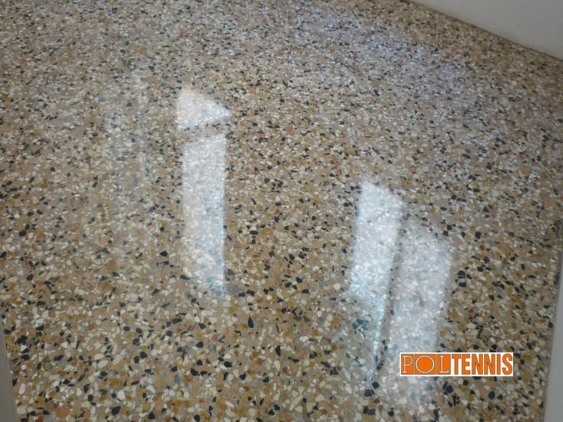 Un pavimento in resina epossidica lucida, con una texture screziata nei toni del beige, del marrone chiaro e del nero, che riflette la luce proveniente dalle finestre sovrastanti.