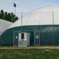 Dietro una recinzione verde si ergono due strutture sportive bianche a forma di cupola, con un piccolo chiosco d'ingresso al centro.
