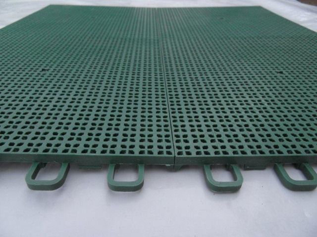 Due piastrelle da pavimento in plastica verde ad incastro con motivo a griglia perforata, posate su una superficie bianca.