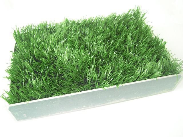 Un contenitore rettangolare riempito di fili d'erba artificiale di un verde brillante su sfondo bianco.