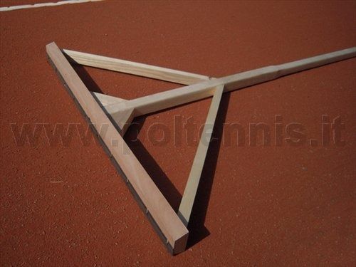 Una spazzola di legno per campi da tennis giace su una superficie di terra battuta rossa.