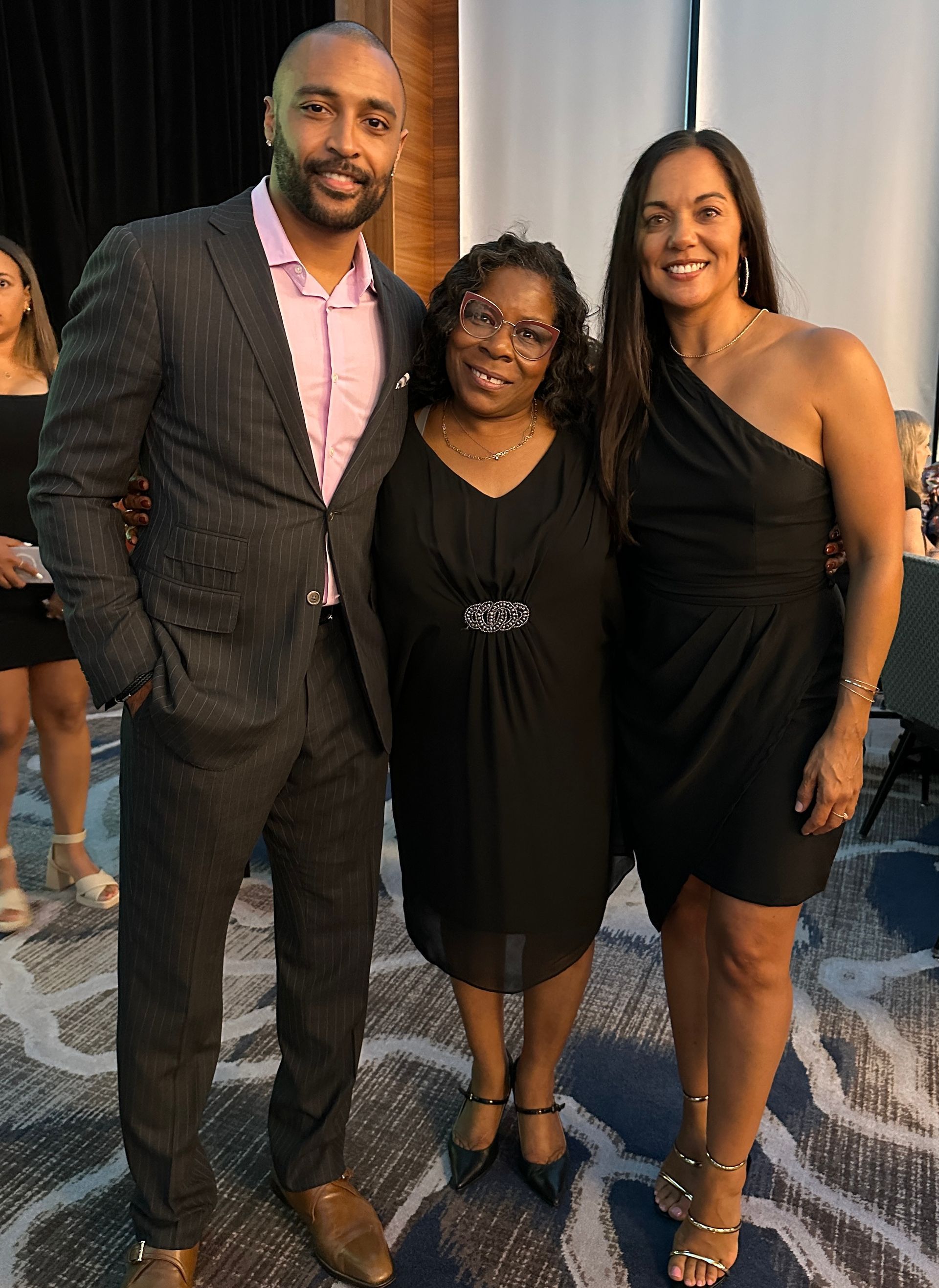 A man in a suit and two women in black dresses are posing for a picture.