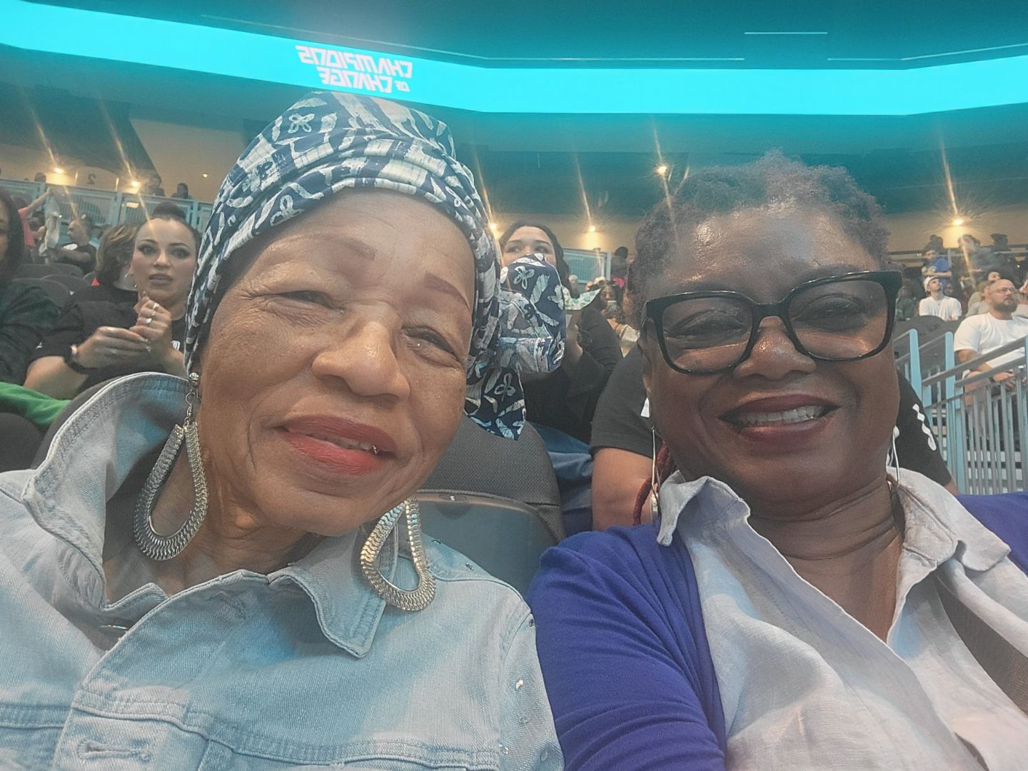 Two women are sitting next to each other in a stadium taking a selfie.