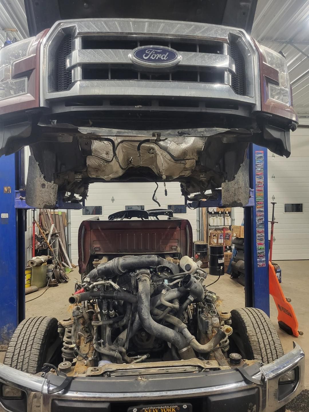 A ford truck is being worked on in a garage with the hood up.