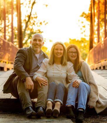 A family is posing for a picture while sitting on a bridge.